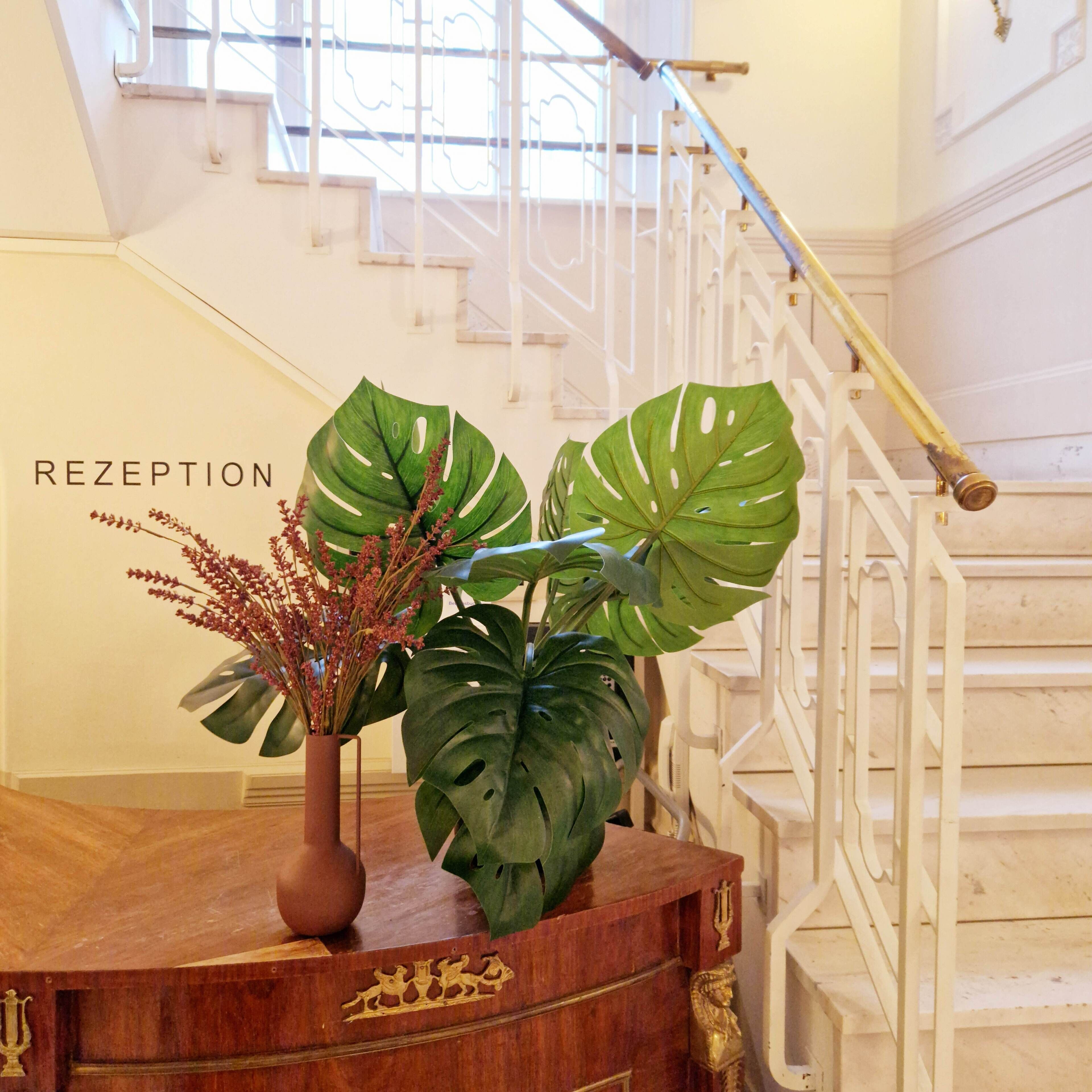 A reception desk with a large Monstera plant and a vase of flowers.