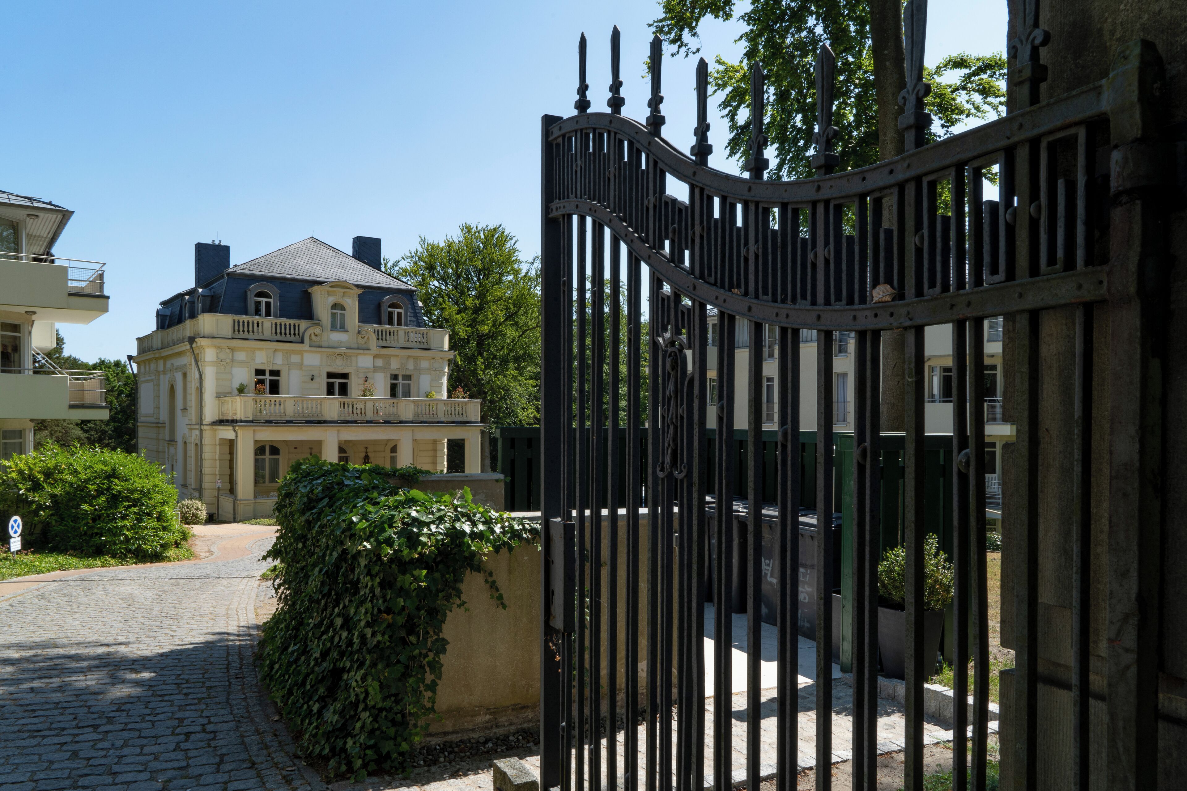 A gated entrance with a cobblestone path leading to a building with a classical facade and a balcony.