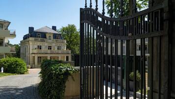 A gated entrance with a cobblestone path leading to a building with a classical facade and a balcony.