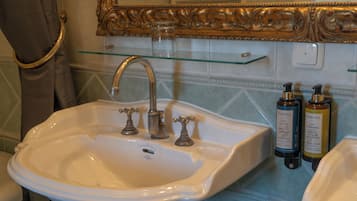 A bathroom with a white sink, two faucets, a glass shelf above the sink, and two bottles of lotion on the wall.