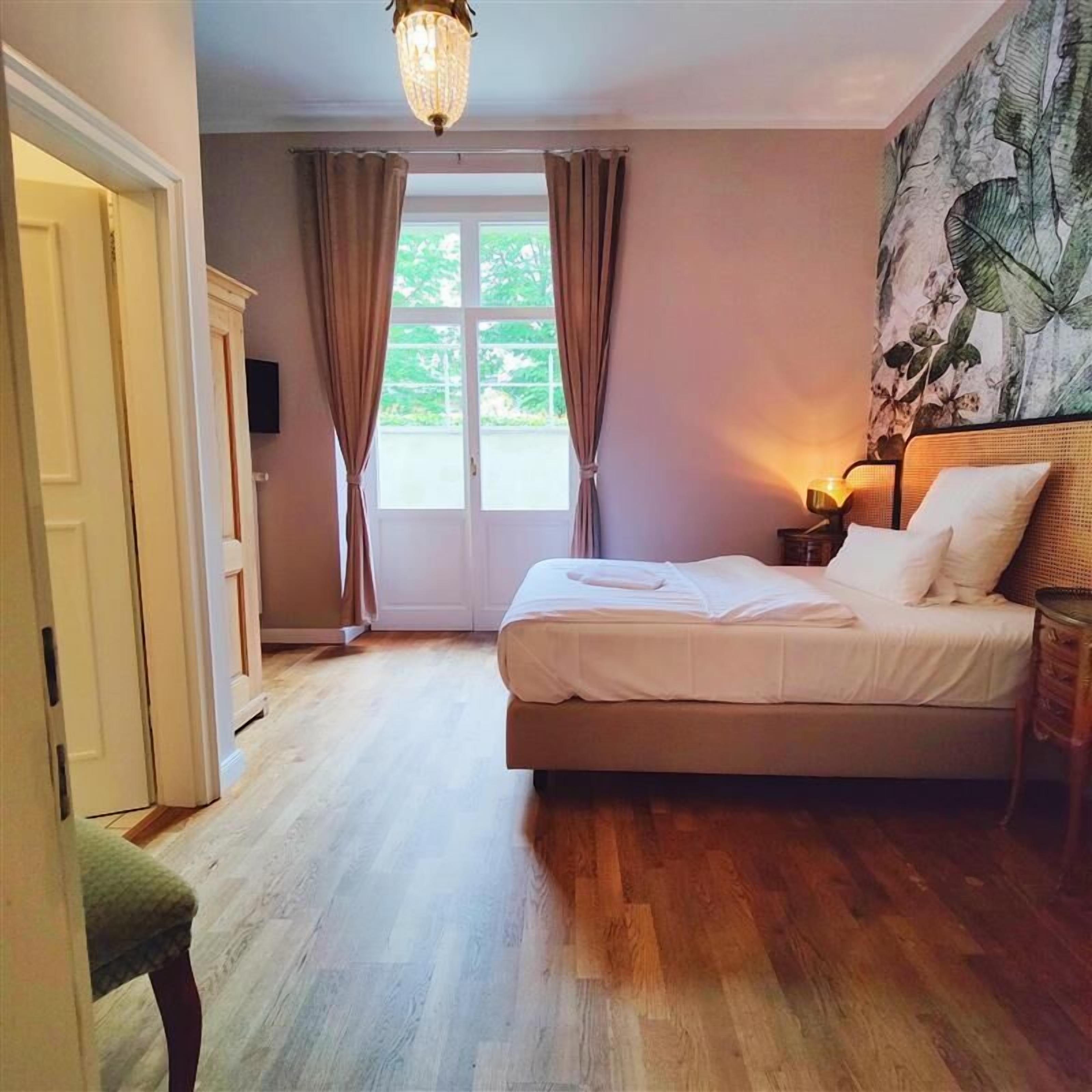 A bedroom with a bed, a nightstand, a lamp, a chair, and a door.