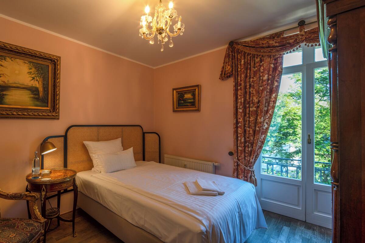 Une chambre à coucher comprenant un lit, une chaise, une table, un lustre et deux tableaux.