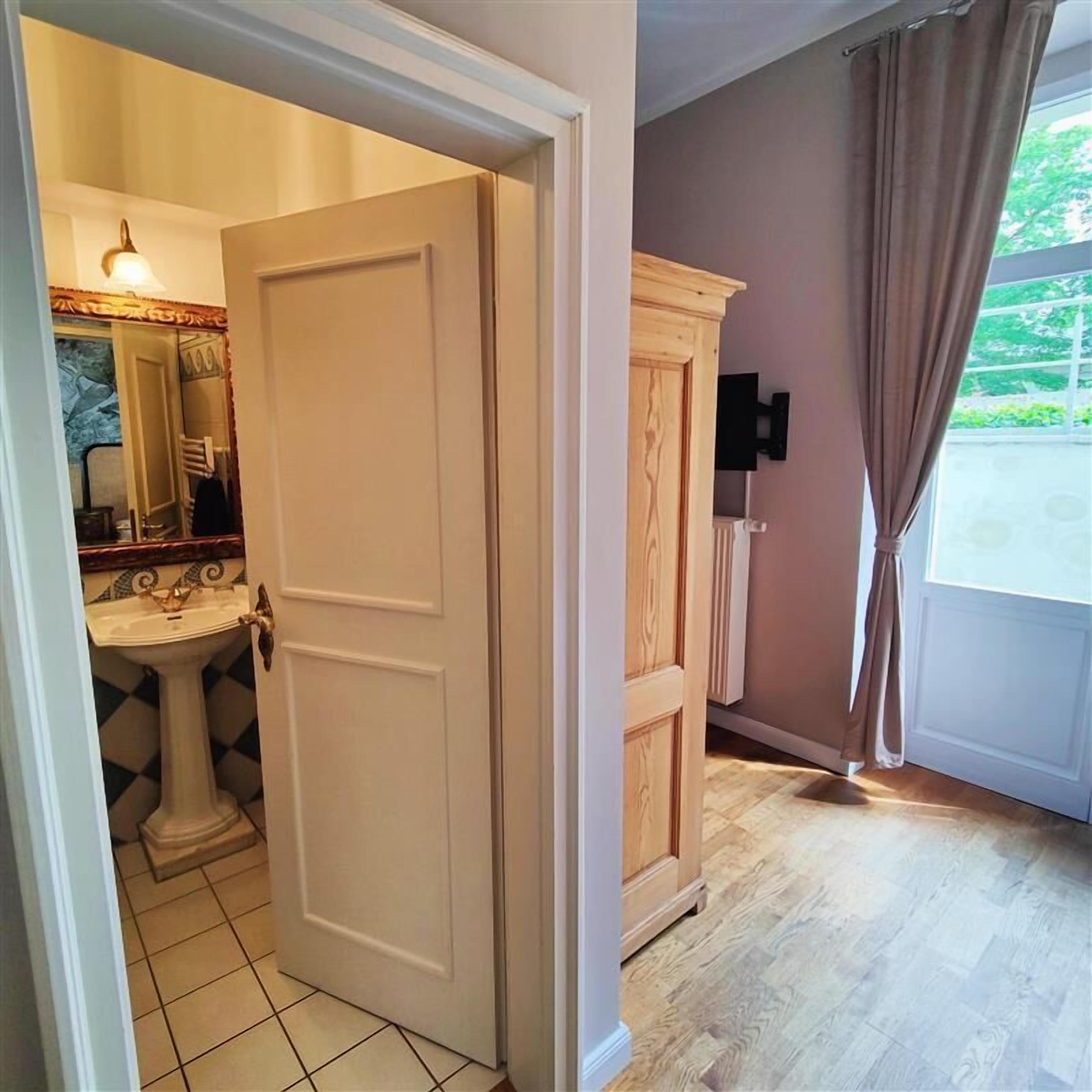 Una habitación con una puerta blanca, un armario de madera y un baño con lavamanos y espejo.