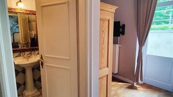 Una habitación con una puerta blanca, un armario de madera y un baño con lavamanos y espejo.