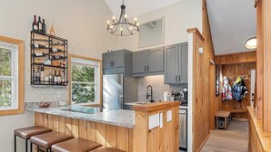 A modern kitchen with wooden accents, a wine rack, and a bar area with stools. - White Mountains Chic Chateau: Updated 3BR+Loft, Sauna, Fireplace & Resort Perks (Campton)