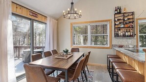 A dining area with a wooden table and chairs, a chandelier, and a wine rack with bottles and glasses. - White Mountains Chic Chateau: Updated 3BR+Loft, Sauna, Fireplace & Resort Perks (Campton)