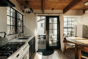 A kitchen with a gas stove, a sink, and a dining area with a table and chairs. - Rou's Cabin Getaway (Running Springs)