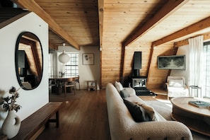 A cozy cabin interior with a wooden ceiling, a sofa, a round table, a fireplace, and a large mirror. - Rou's Cabin Getaway (Running Springs)
