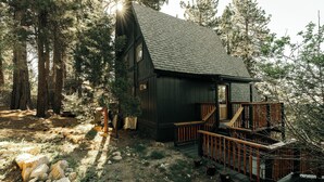 Eine Holzhütte mit einer Holzdar Terrasse, umgeben von Bäumen und felsigem Untergrund.