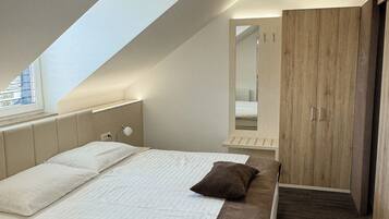 Un dormitorio moderno con techo inclinado, una cama grande con ropa blanca, un plaid marrón, un armario de madera y un tragaluz.
