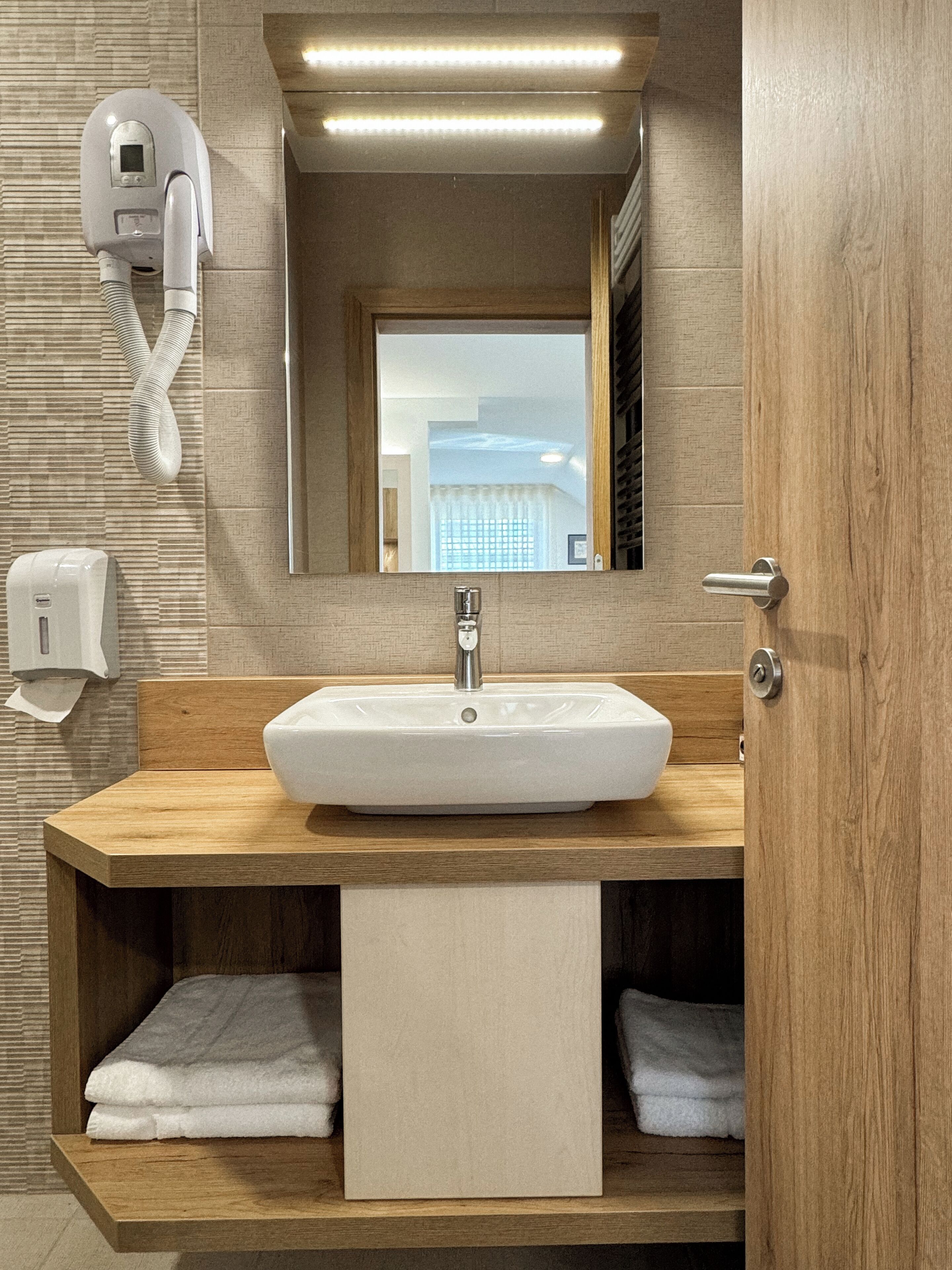 A modern bathroom with a large sink, a mirror, a towel rack, and a hand dryer.