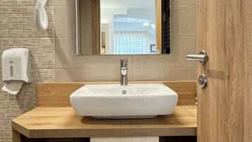 A modern bathroom with a large sink, a mirror, a towel rack, and a hand dryer.