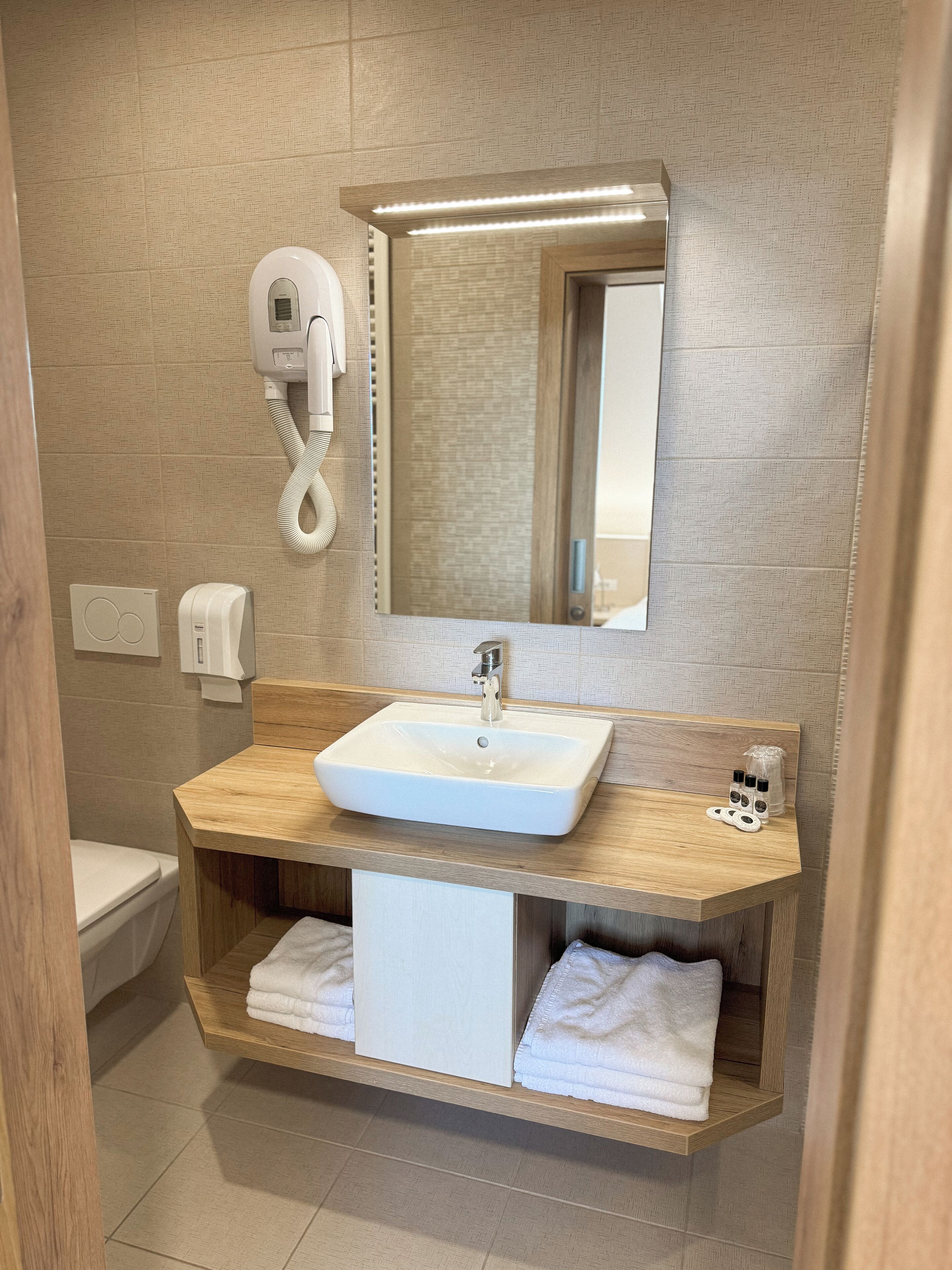 A modern bathroom with a wooden vanity, a white sink, a mirror, and a towel rack.