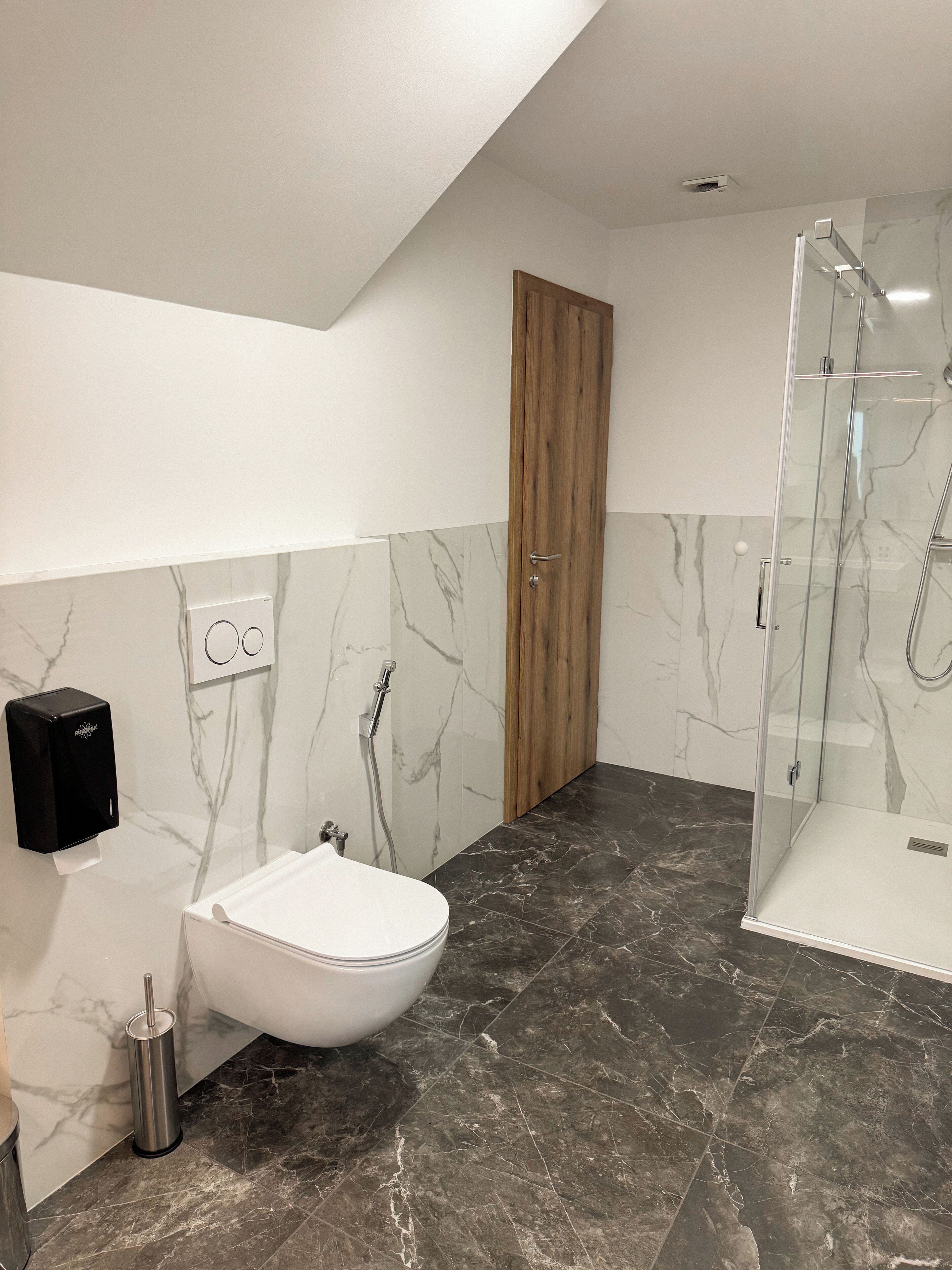 A modern bathroom with a white toilet, a bidet, a glass-enclosed shower, and marble walls.