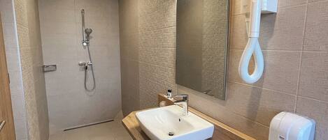 Un bagno moderno con un mobile bagno in legno, uno specchio grande, un soffione a mano e un porta asciugamani.