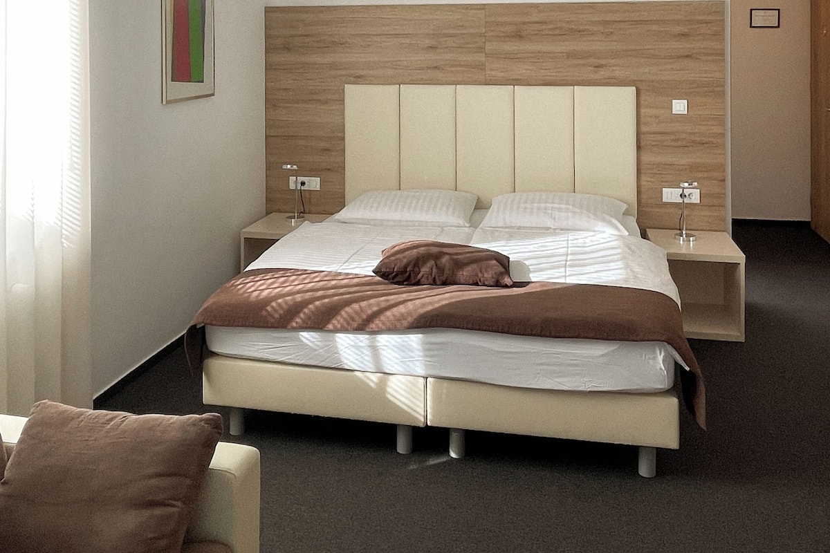 Moderni hotellihuone, jossa on suuri sänky, yöpöydät ja neutraali värimaailma.