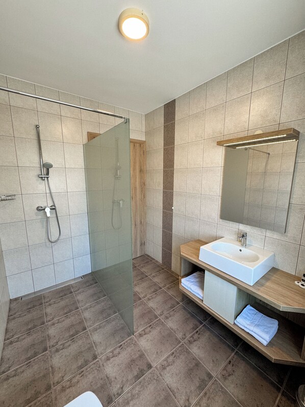 A modern bathroom with a glass-enclosed shower, a wooden vanity with a sink, and a mirror above it.