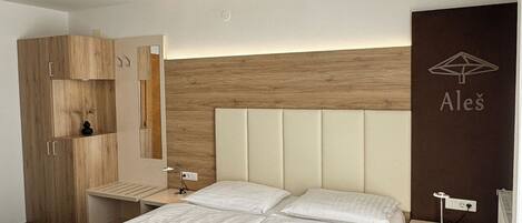 A modern hotel room with a large bed, a wooden wardrobe, a bedside table, and a wall-mounted shelf.