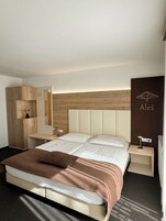 Una habitación de hotel moderna con una cama grande, un armario de madera, una mesita de noche y una estantería de pared.