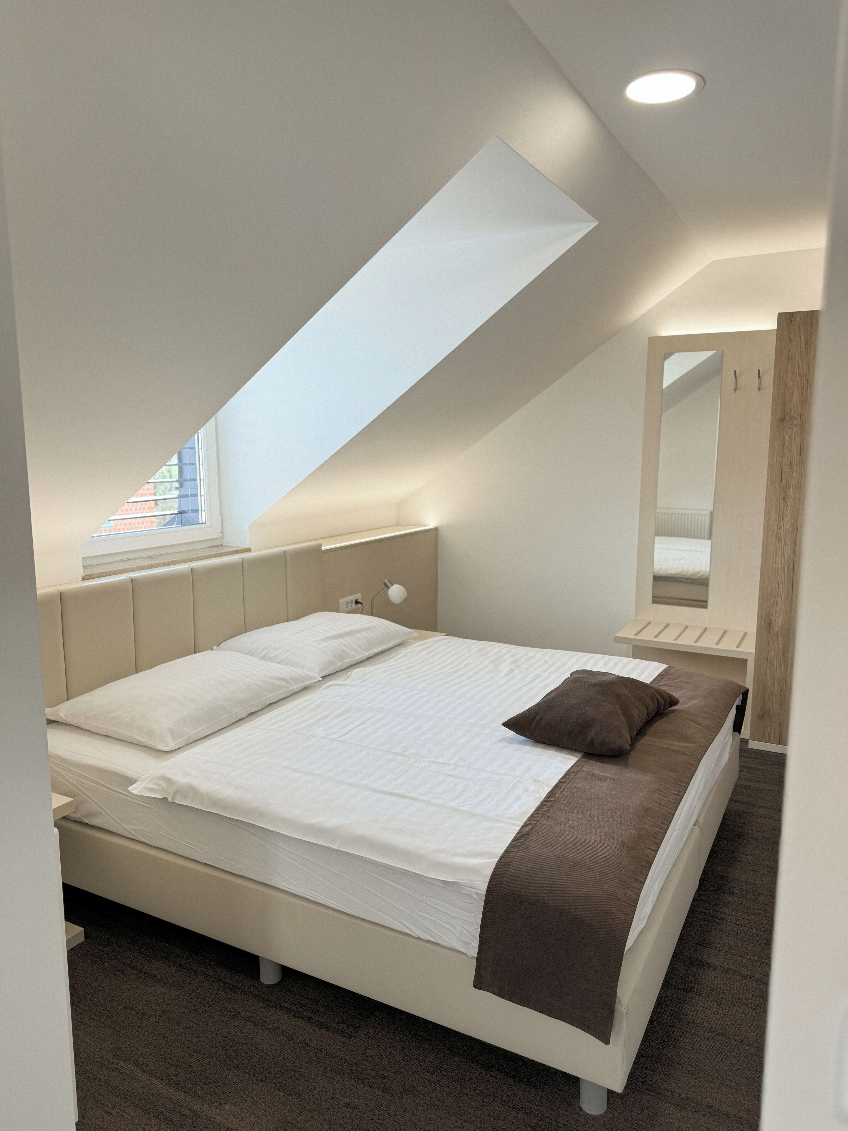 Una camera da letto moderna con soffitto a falde, un lucernario, un letto con biancheria bianca e marrone e un grande specchio.