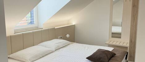 Una camera da letto moderna con soffitto a falde, un lucernario, un letto con biancheria bianca e marrone e un grande specchio.