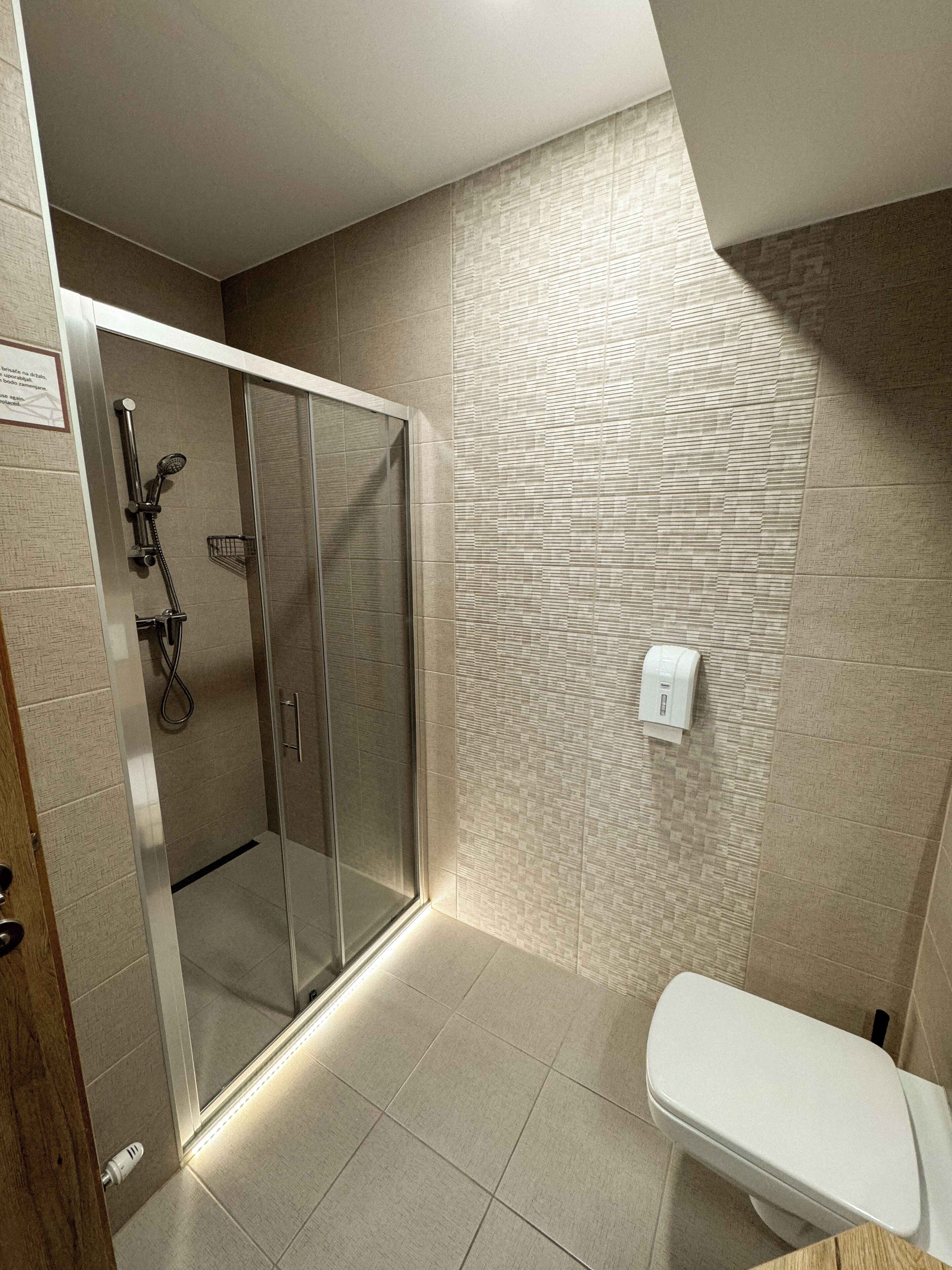A modern bathroom with a glass-enclosed shower, a toilet, and a wall-mounted hand dryer.