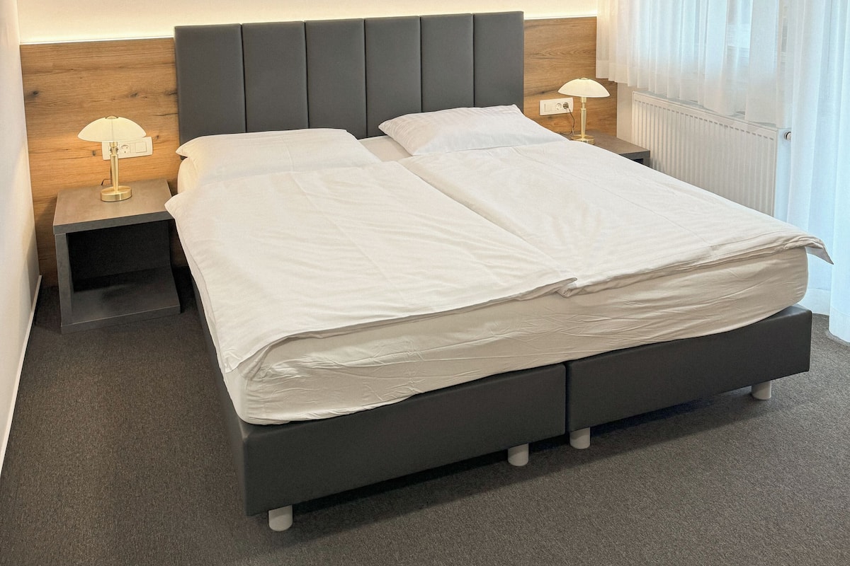 Moderni hotellihuone, jossa on suuri sänky, yöpöydät ja kattovalaisin.