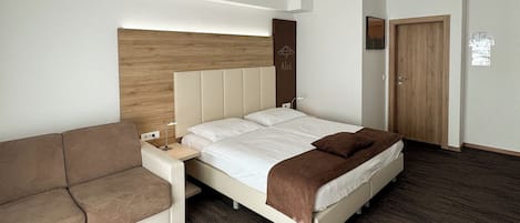 A modern hotel room with a bed, a sofa, a wooden headboard, and a door.