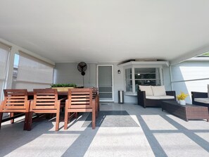 Un patio techado con una mesa y sillas de comedor, un rincón de estar con cojines y un ventilador.