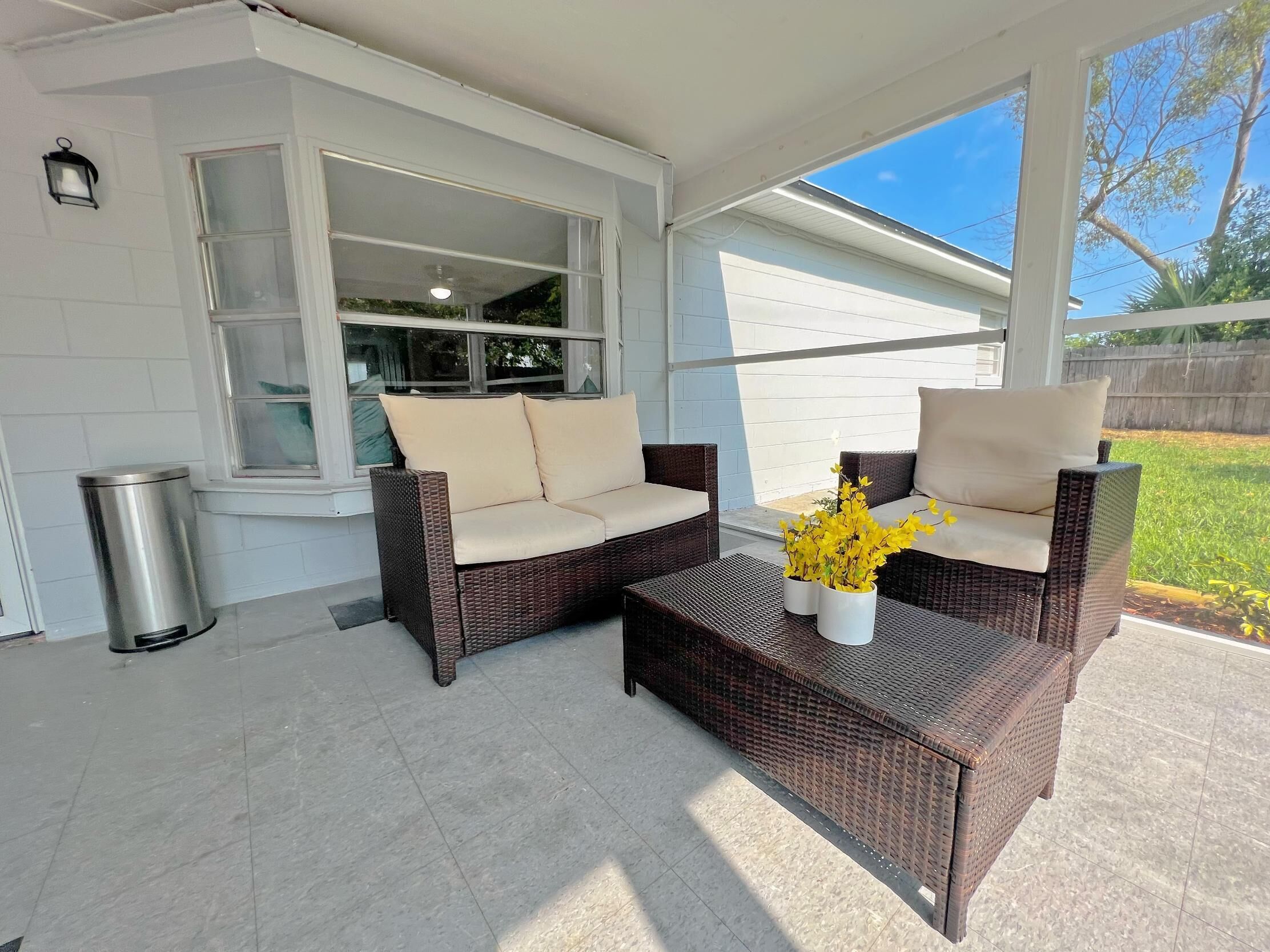 A covered patio area with wicker furniture and a trash can.
