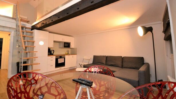 A modern living room with a sofa, red chairs, a glass coffee table, a remote control, and a kitchen in the background. - Loft Piccadilly Circus Apartment (London)