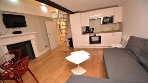 A modern living room with a grey sofa, a white coffee table, and a red chair. A kitchen area with white cabinets and a microwave is visible in the background. - Loft Piccadilly Circus Apartment (London)