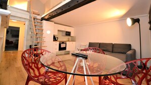 A modern living room with a glass dining table, red chairs, a sofa, and a staircase leading to an upper level. - Loft Piccadilly Circus Apartment (London)