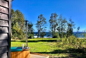 A wooden deck with a hot tub, a metal pole, and a view of the ocean. - Calma Cabins (Puerto Octay)