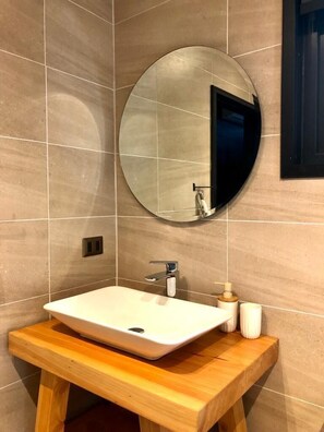 A bathroom with a white sink, a round mirror, and a wooden vanity. - Calma Cabins (Puerto Octay)