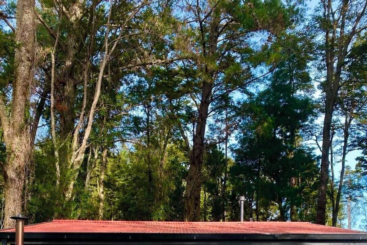 A covered outdoor area with a hot tub, seating, and a view of surrounding trees.