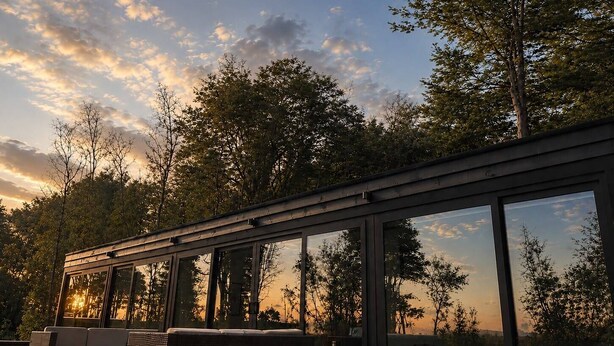 A modern outdoor deck with a sofa and chairs, large glass windows, and a view of trees and sky. - Calma Cabins (Puerto Octay)
