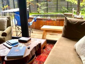 Een gezellige zithoek met een bank, een bijzettafeltje met boeken en uitzicht op een tuin en zwembad.