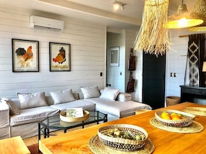 A living room with a sofa, coffee table, and a dining table with baskets of fruit.