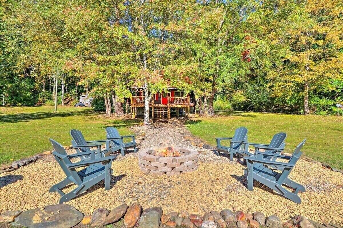 A cabin with a fire pit and Adirondack chairs in a forest setting.