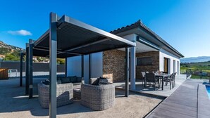 Eine überdachte Terrasse mit Korbmöbeln, einem Pool und einer Steinmauer.
