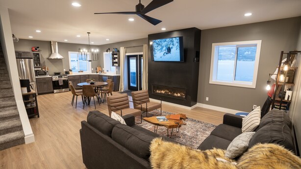 A modern living room with a fireplace, a television, and a dining area. - Teton Basecamp Barndominium (Driggs)
