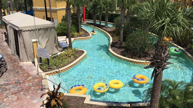 A pool area with a tiled floor, palm trees, and inflatable rings. - HOME AWAY FROM HOME -VACATION VILLA  (Kissimmee)