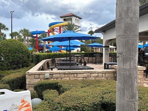 Relax in a shaded outdoor seating area surrounded by lush greenery and a vibrant water slide.