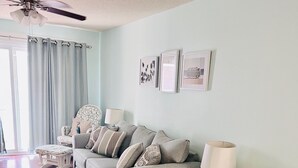 A living room with a grey sofa, a green armchair, and a white side table with a lamp. There are framed pictures on the wall and a ceiling fan above. - Walk Across the Street to Beautiful Soft Sandy Beach! (Murrells Inlet)
