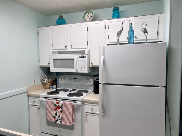 A kitchen with white cabinets, a microwave, a stove, and a refrigerator. - Walk Across the Street to Beautiful Soft Sandy Beach! (Murrells Inlet)