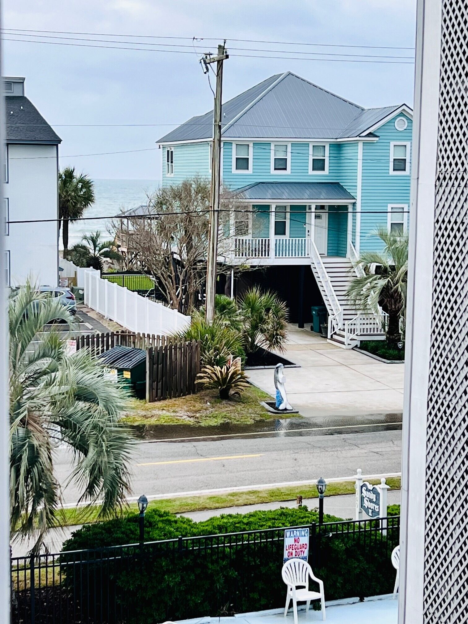 A coastal house with a porch, a lifeguard duty sign, and a chair outside.