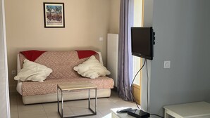 Una sala de estar con un sofá, una mesita, un televisor montado en la pared y una ventana con cortinas.