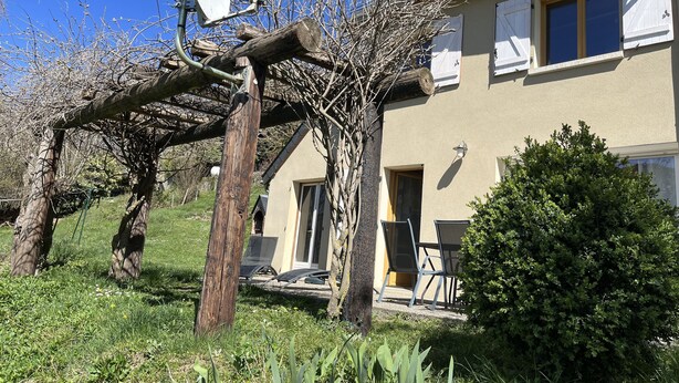 Una casa con antena parabólica, una pérgola y un jardín con sillas.