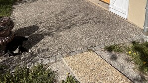 Un edificio con camino de grava, contraventanas blancas y puerta de madera.